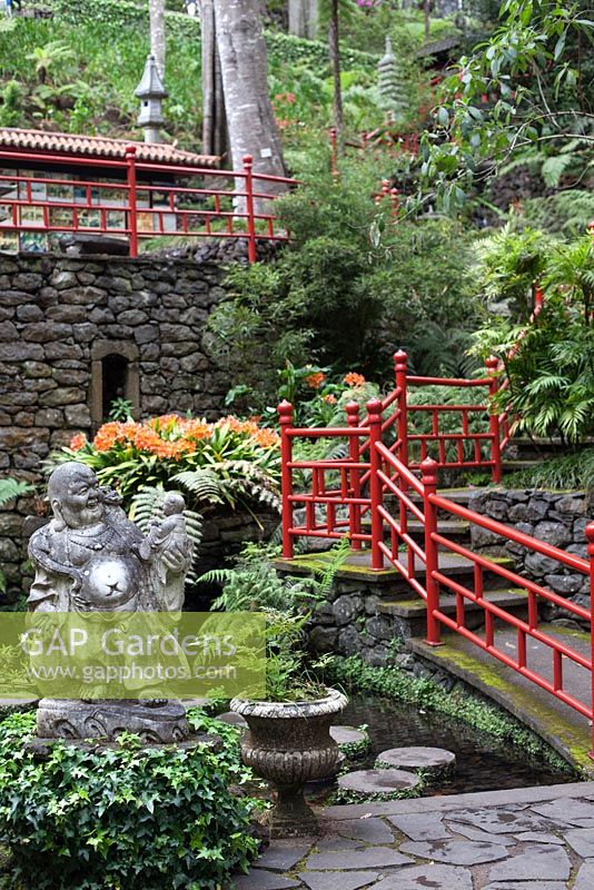 Clivia miniata with Buddha statue in Oriental garden at Monte Palace Tropical Garden, Madeira, with red railings