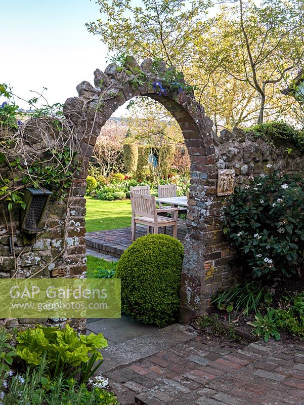 A stone arch provides the entrance to the rear of an English country garden in spring.