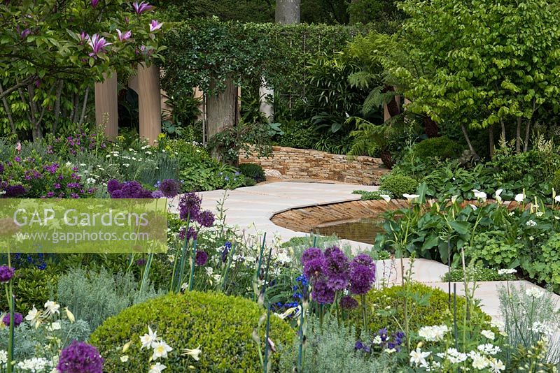 The Time In Between by Husqvarna and Gardena. View over bed of allium, aquilegia, anchusa, geranium and box balls to pool edged in curving stone path and sunken seating area.