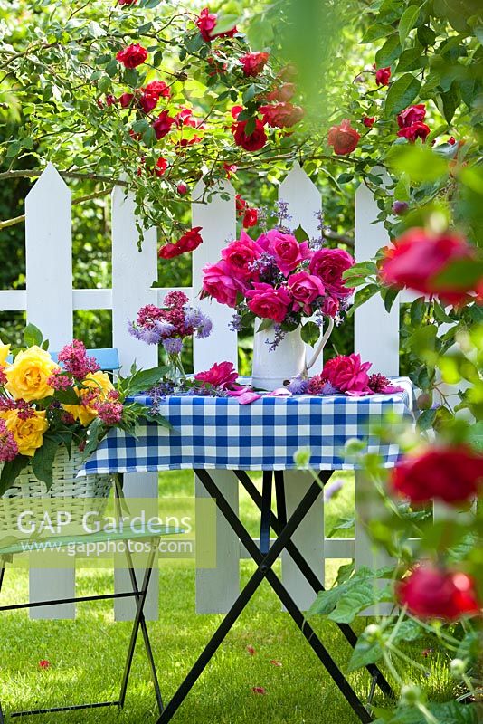 Cut flower arrangement with roses on garden table in summer. Rosa 'Crimson Glory' - climbing rose