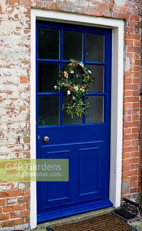 A festive wreath made from Holly, Ivy, Mistletoe and Pine cones hanging on a blue door