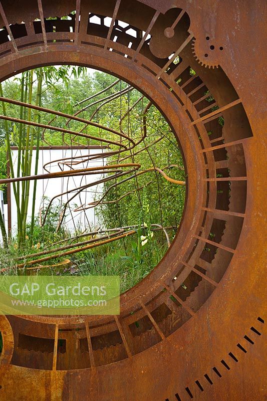 A rusted corten steel oculus and warped steel rods depicting the trajectory of light flow through the garden planted with foliage plants including Phyllostachys and grasses. Dark Matter Garden for the National Schools' Observatory. 
