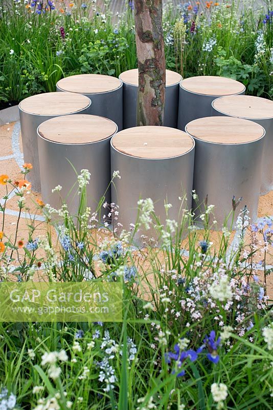 Thinking of Peace by Lace Landscapes. Cylindrical seating made from steel and wood, surrounded by borders containing Iris sibirica 'Tropical Night' and 'Blue King', Veronica 'Pallida', Amsonia tabernaemontana, Luzula nivea. 