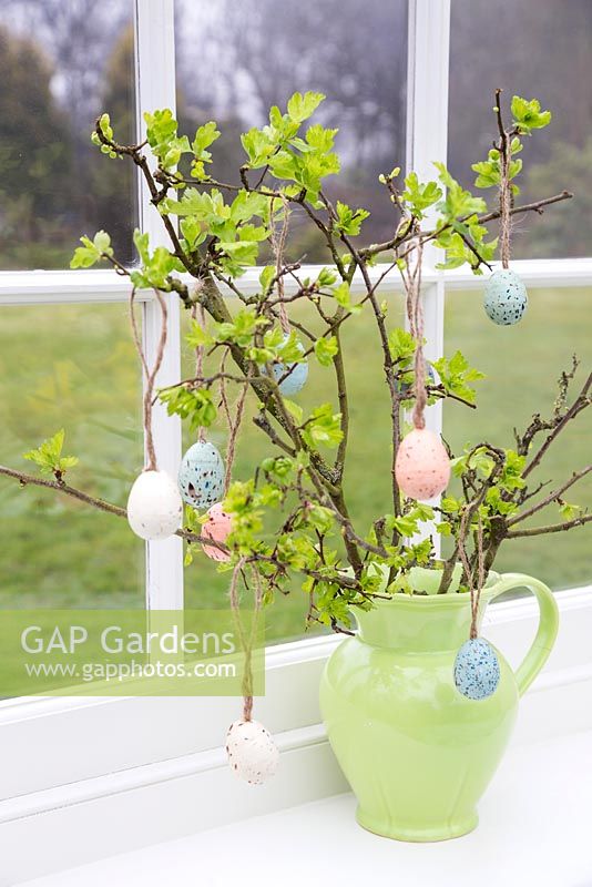 Floral display containing fresh spring foliage and decorative eggs, with a view to the garden