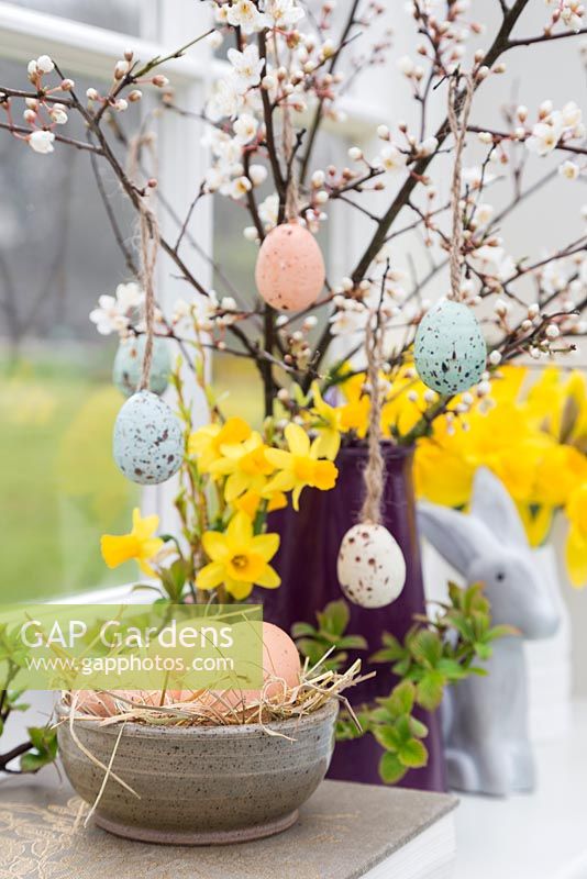 Floral display containing decorative eggs, Daffodils, Blossoming spring foliage and a Bunny, with a view to the garden