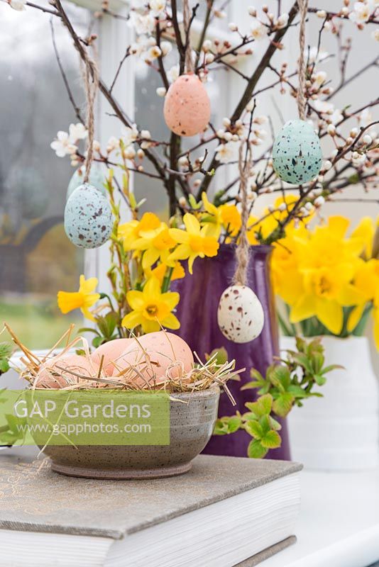 Floral display containing decorative eggs, Daffodils and blossoming spring foliage, with a view to the garden
