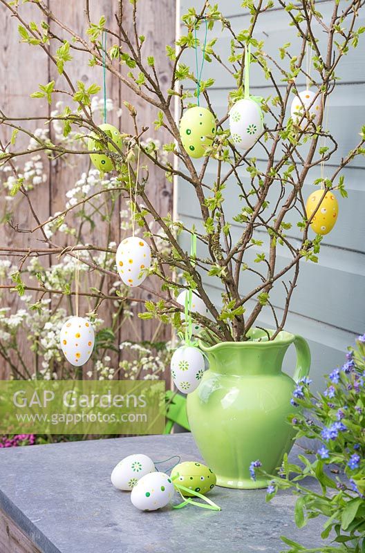 Decorative eggs hanging from fresh spring foliage in a green jug
