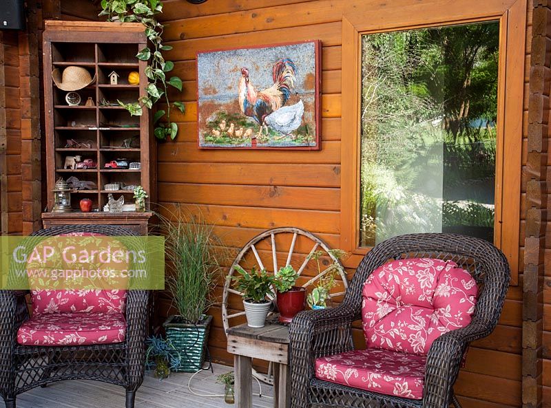 Seating area shelves and artwork on veranda of wooden cabin style house. Containr planting includes, Epipremnum sp, MIscanthus sinensis 'Gracillimus', Sempervivum, Senecio, Schlumbergera 