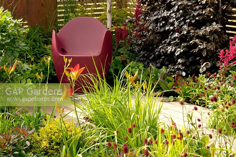 Wooden decking with chair and mixed flower borders with Fagus sylvatica, Sanguisorba officinalis 'Morning Select', Astilbe x arendsii Fanal', Bergenia and Hemerocallis 'Lusty Lealand' in Foundations for Growth at  RHS Hampton Court Palace Flower Show 2015.  