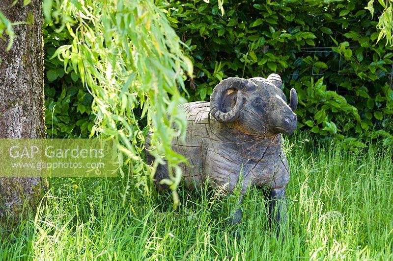 Wooden sculpture of a sheep beneath a willow tree.