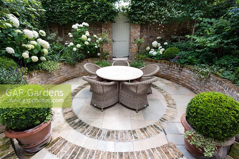 Walpole Gardens: London. View onto circular tile and brick sunken patio with Carpinus betulus, Hydrangea arborescens 'Annabelle', Salvia 'Caradonna', Erigeron karvinskiansus, Heuchera 'Rave On', Buxus sempervivens