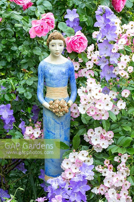 Blue ceramic lady holding a flower bouquet next to Rosa 'Ballerina', 'Leonardo da Vinci', Buxus and Campanula persicifolia var. sessiliflora