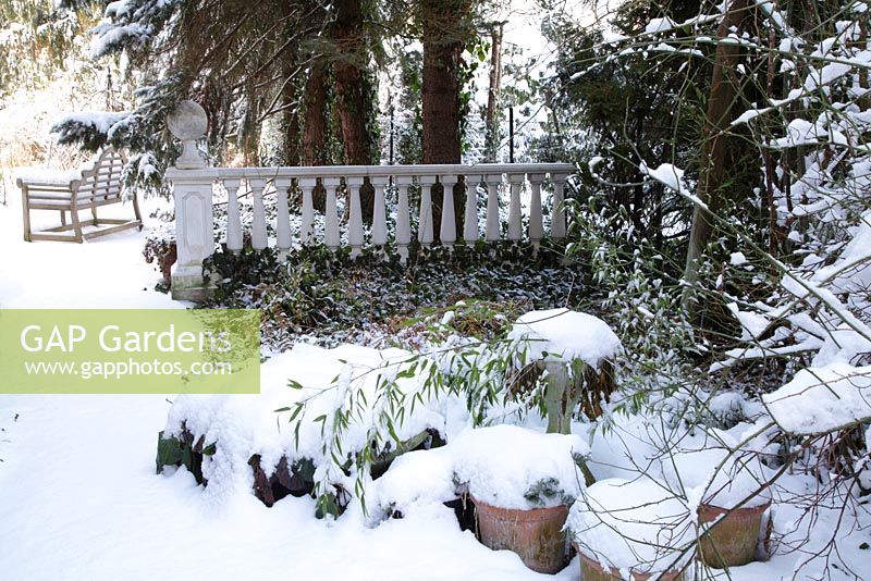 Winter scene with balustrade, wooden bench, plants in pots covered with leafes and snow - Welsch Garden, Berlin, Germany