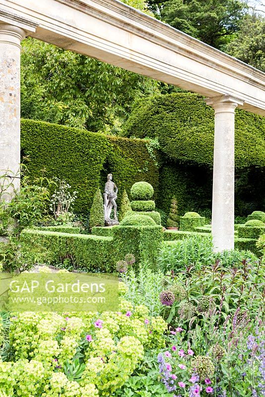 Formal garden next to the Great Terrace colonnade and Casita. Hedges and topiary of Buxus sempervirens. Clipped Yew behind. Terracota pot from Italy. Iford manor, Bradford-on-Avon, Wiltshire. July. Garden designed and created by Harold Peto. Historic garden grade I.