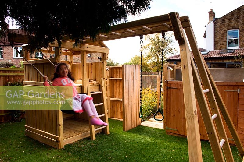 Girl on swing in children's play area with wooden climbing frame. Small urban contemporary town garden.  Artificial grass surface. Ansari garden, Harrow