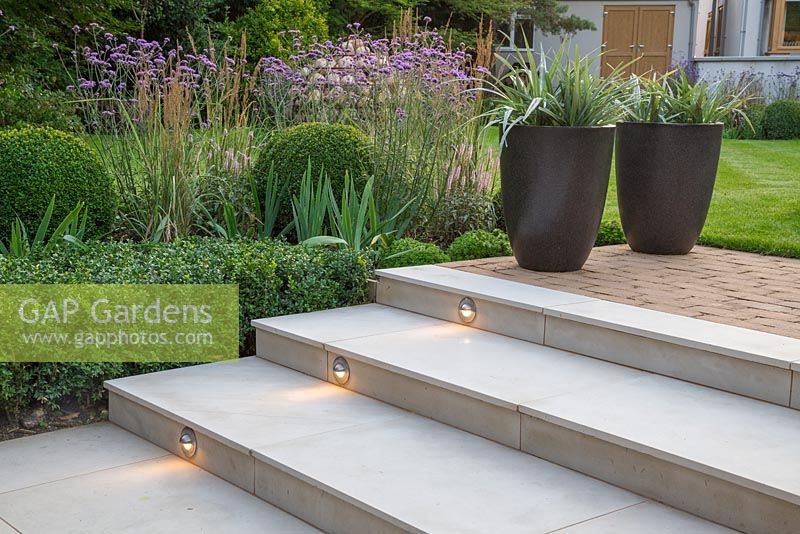 View of lighting feature built into marble steps, with border of Verbena bonariensis, Buxus sempervirens hedge and spheres, Veronica and Calamagrostis x acutiflora 'Karl Foerster'. Potted Astelia chathamica