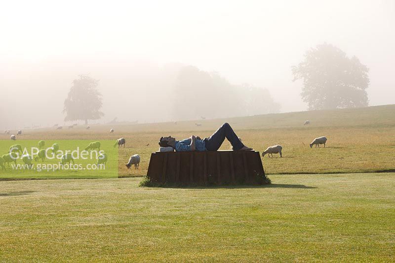 The main lawn in mist with bronze and corten steel sculpture by Sean Henry.  Sheep grazing in field beyond. 