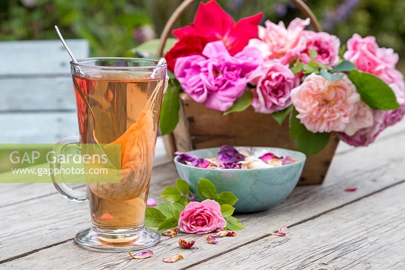 A glass of Rose tea with a trug of cut Roses and petals