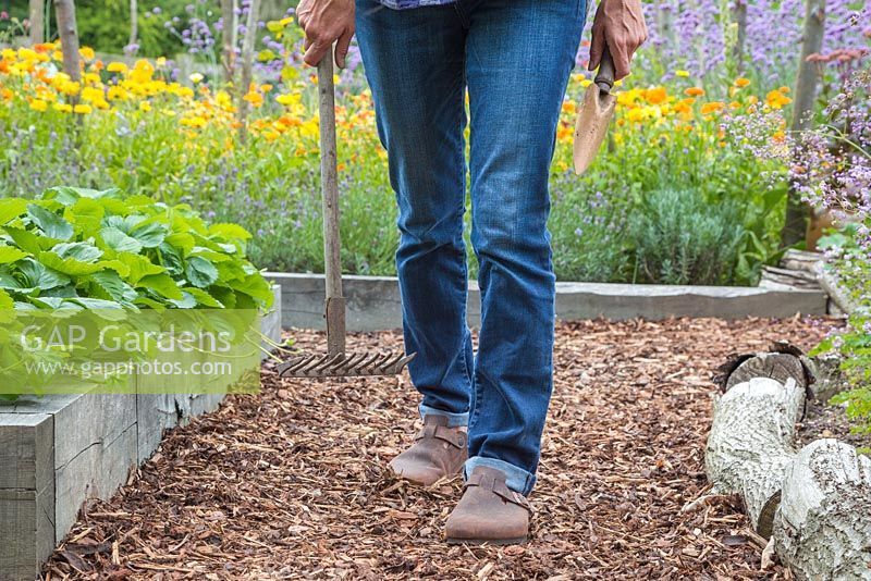 Woman walking down path of bark chippings mulch carrying garden tools