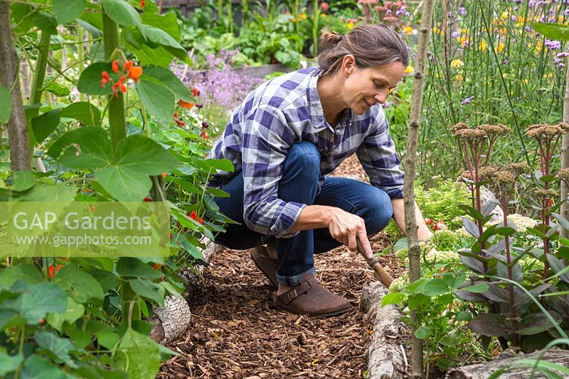 A woman carrying out some weeding in a bed beside a path of bark chippings mulch