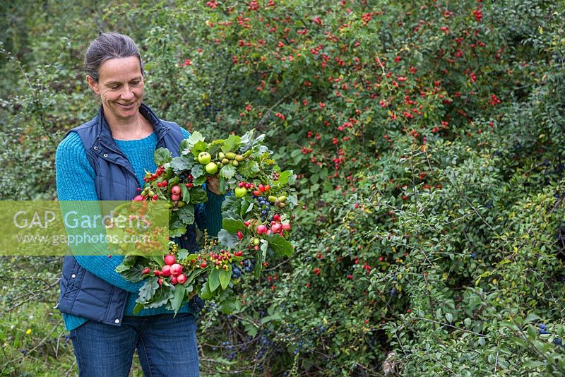 Woman holding an Autumnal Berry wreath featuring Wild Crab Apples, Hawthorn - Crataegus, Sloe berries - Prunus spinosa, Rose hips, English Oak - Quercus robur and Crocosmia seed heads