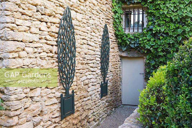 Garden in Luberon, France, Designed by Michel Semini: wooden trompe l'oeil trees in containers on wall beside the back door