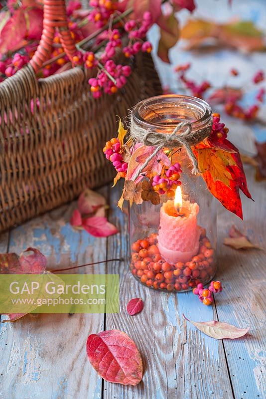 A glass jar candle holder decorated with autumnal foliage, Spindle and Pyracantha berries