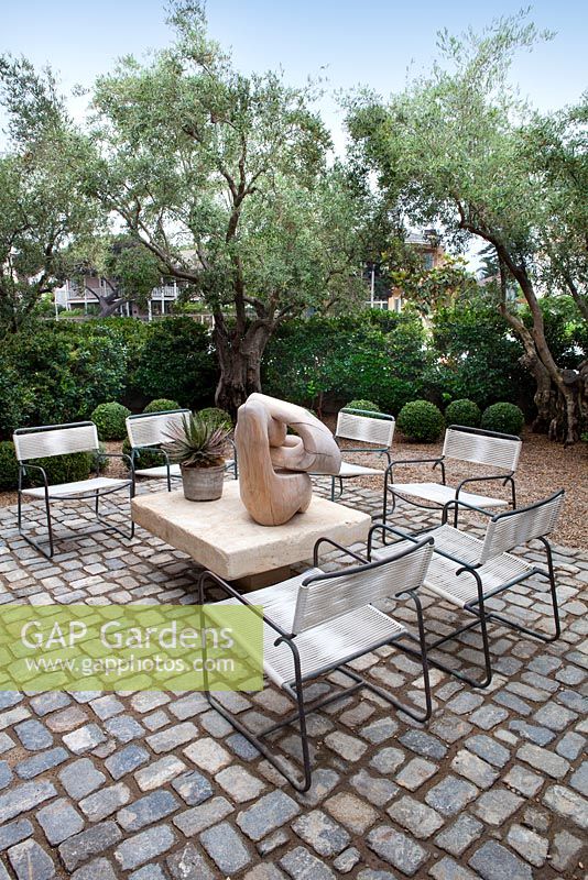 View of cobbled outside seating area with chairs and wooden sculpture with gravel garden beyond.
