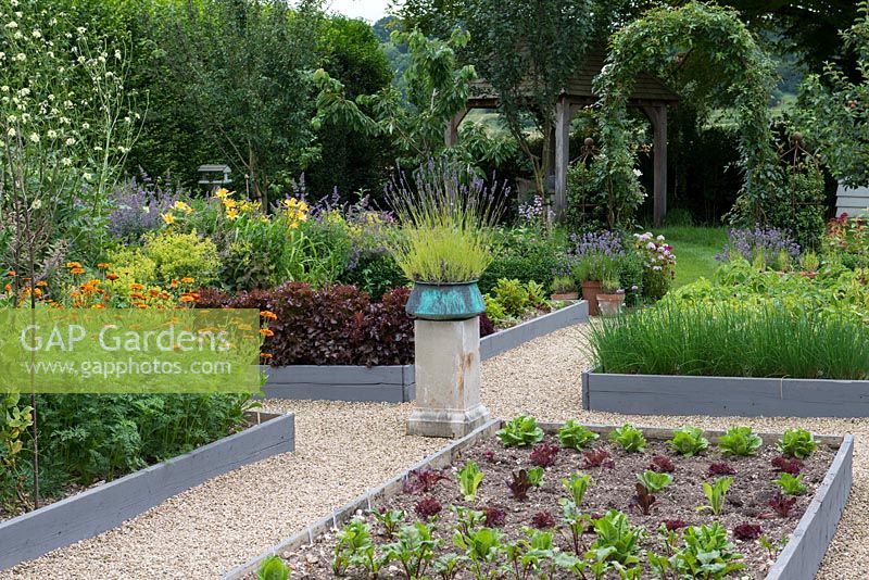 A potager with raised beds of chives and salad. A stone plith with a copper pot of  lavender provides a focal point on the central axis.