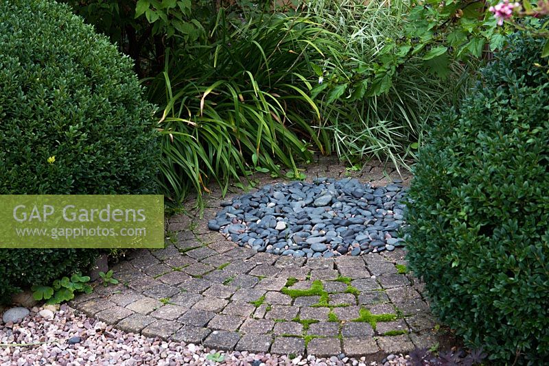 Pebbles, paving and box balls combined in a garden with a circular theme.