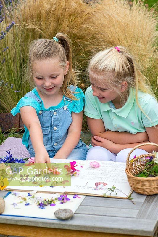 Two little girls, aged 6 and 9, pressing garden flowers in an old nursery rhyme book.
