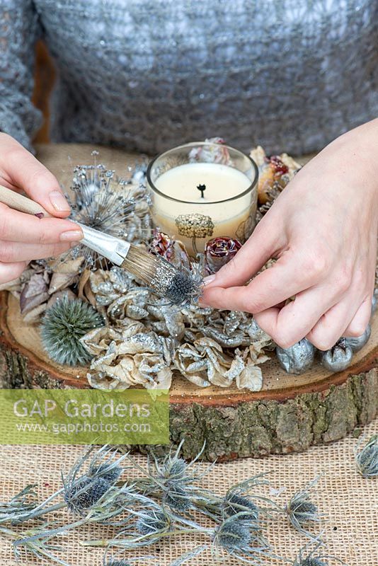 Creating a festive table decoration with garden flowers and seed heads. Paint silver glitter onto sea holly seed heads.