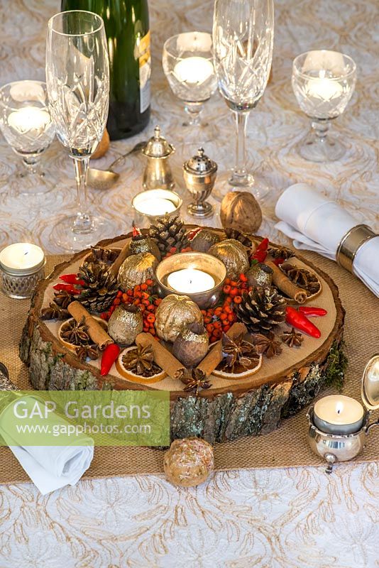A candle-lit festive table decoration with dried fruit, nuts, seeds, with freshly picked berries and chilli peppers.