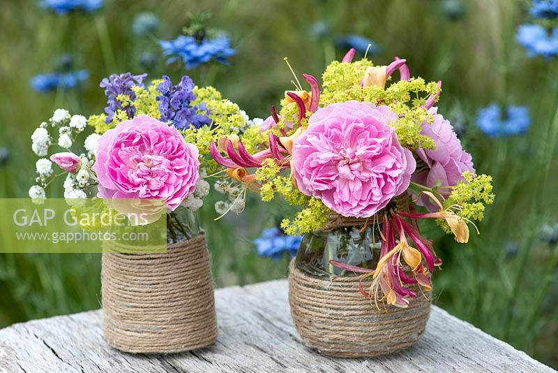 Colourful summer posies with pink rose, alchemilla, baby's breath, honeysuckle and catmint in glass jars decorated with twine.