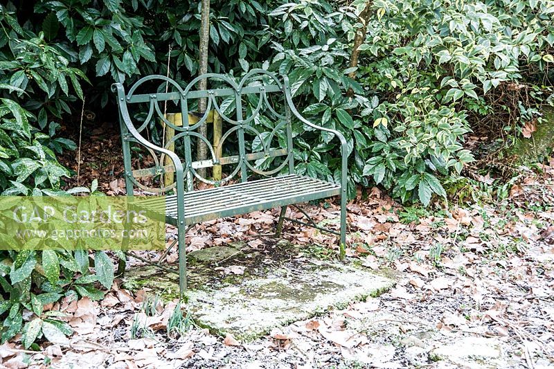 Green metal bench in a garden dusted with a light icing of snow. Dorset, UK