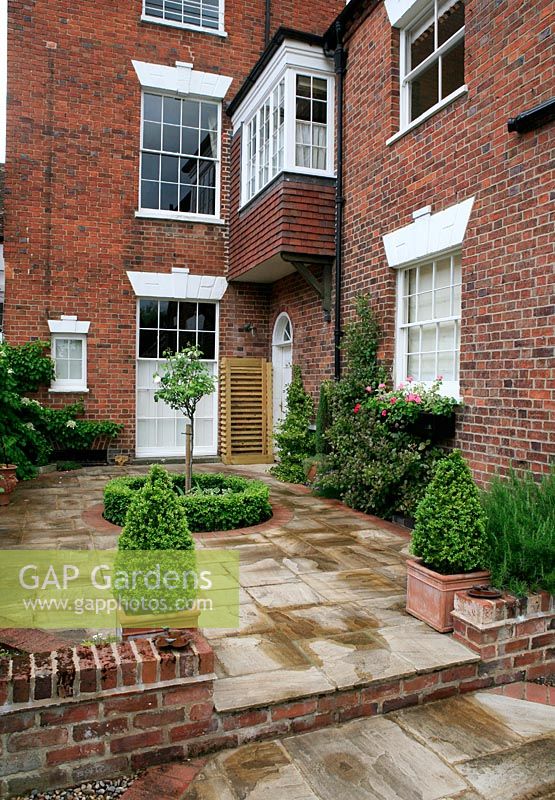 Small formal, low maintenance courtyard garden with clipped box in containers and a central, circular bed. The terrace is laid in Indian sandstone and retaining walls and step riser built with salvaged bricks to match the period house. 