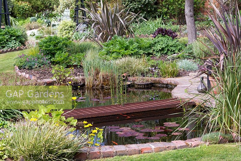 A brick edged fish pond with rusted metal bridge.