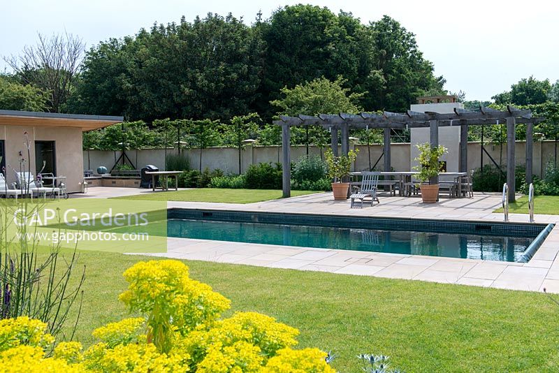 A paved seating area and wooden pergola beside a swimming pool.