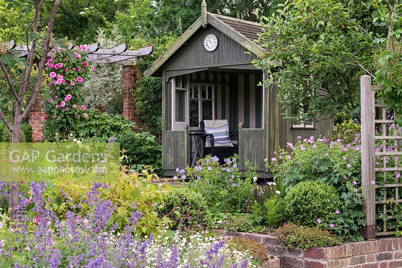 A summer garden with mixed borders including catmint, geranium and Rosa 'Gertrude Jekyll' surround a rotating victorian summerhouse.