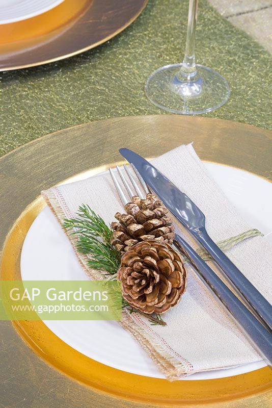 A festive place setting featuring a gold plate with Pine cones and foliage