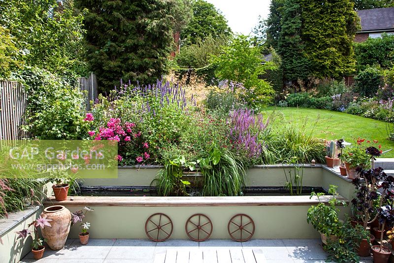 View of back garden showing pots, water feature, Summer borders and lawn. 