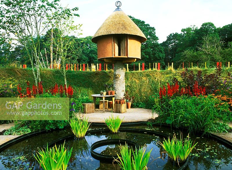 Modern treehouse beside pond - iris, lobelia.      Westonbirt flower festival 2002: The round garden. Designers: Patricia Stainton and Stephen Morgan
