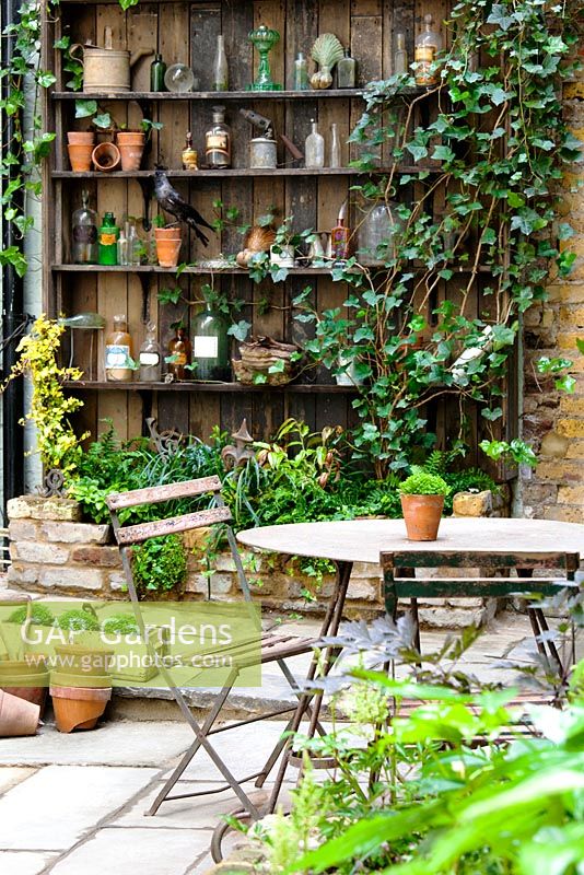 View of court yard with table and chairs to shelves with artefacts. Lucille Lewins, small office court yard garden in Chiltern street studios, London. Designed by Adam Woolcott and Jonathan Smith June 2010, UK