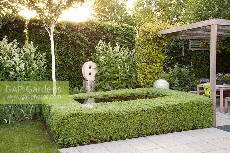 Clipped box hedge around Infinity pool on patio with contemporary statue 'Untitled' by artist Will Spankie, white Astilbe and covered seating area for entertaining 