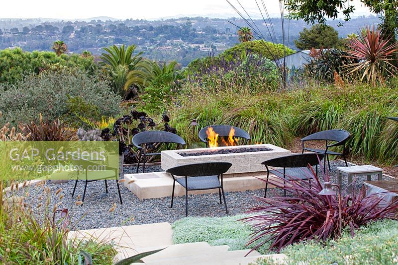 View of gas fired fire pit alight with outside seating. Debora Carl's garden, Encinitas, California, USA. August.