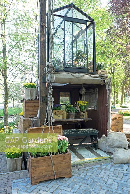 Greenhouse on top of a container. Tiny house in container with classic old aged furniture and pictures. Wooden boxes filled with Narcissus and Hyancinthus. Wooden stair to top. Inspiration garden: Golden Age.