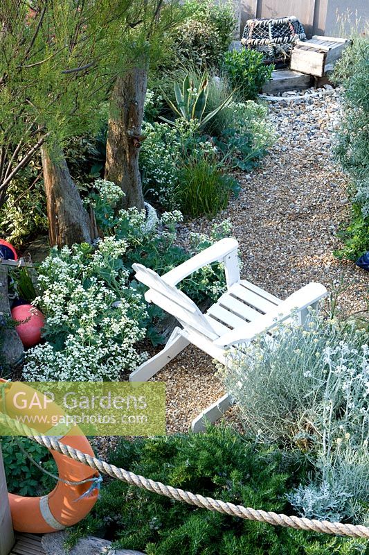Beach themed garden with rope, life belt, white painted seat, crab nets, buoy, crambe maritima, gravel, agave, artemisia and tamarix. 