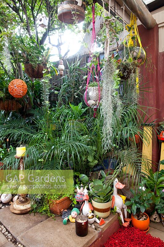 A collection of quirky statues, seabird statues, palms, Spanish Moss, Tillandsia usneoides, succulents, orange plastic lampshade and a birdhouse.