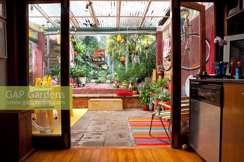 Looking from inside the house to the garden with begonias, ferns and palms features colourful eclectic retro pieces sourced from local markets. 