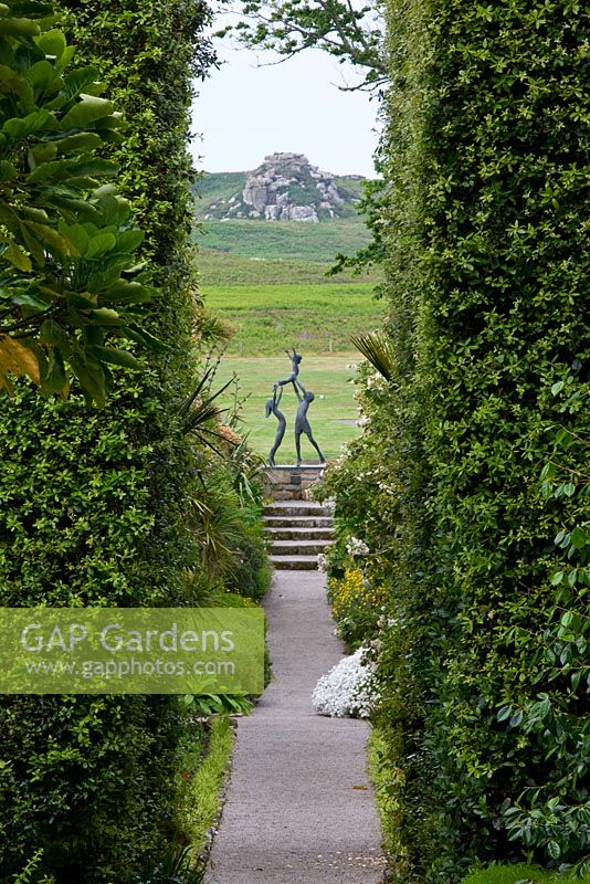View down The Neptune Steps through hedges of Quercus Ilex to sculpture - 'Tresco Children' by David Wynne. Tresco Abbey Gardens, Tresco, Isles of Scilly. 